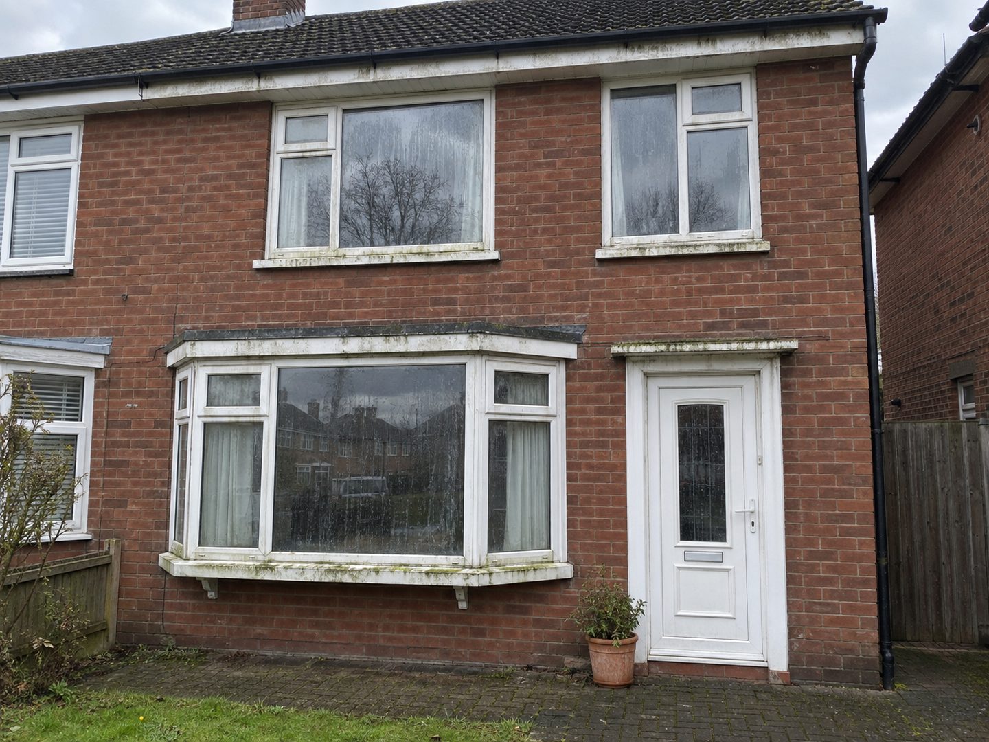 The same house before, with green growth along the frames, sills and bay roof